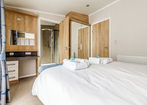 A hotel room with a bed, a desk, a mirror, and a shower area.