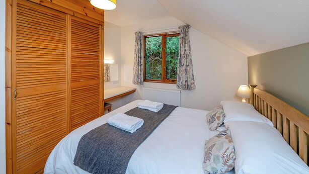 Een slaapkamer met een bed, een houten garderobe, een raam met gordijnen en een lamp.