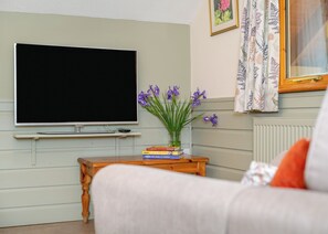 A living room with a flat-screen TV, a small wooden side table with books, a vase with flowers, and a couch. - Timber lodge set in an elevated woodland position with one double and one twin. (Webbery, Bideford)
