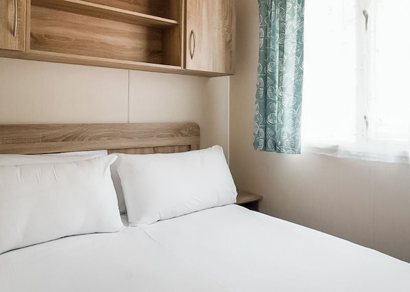 A bed with white bedding, a wooden headboard, and a nightstand with a lamp. - 1 bedroom accommodation in Porth, Newquay (Porth, Newquay)
