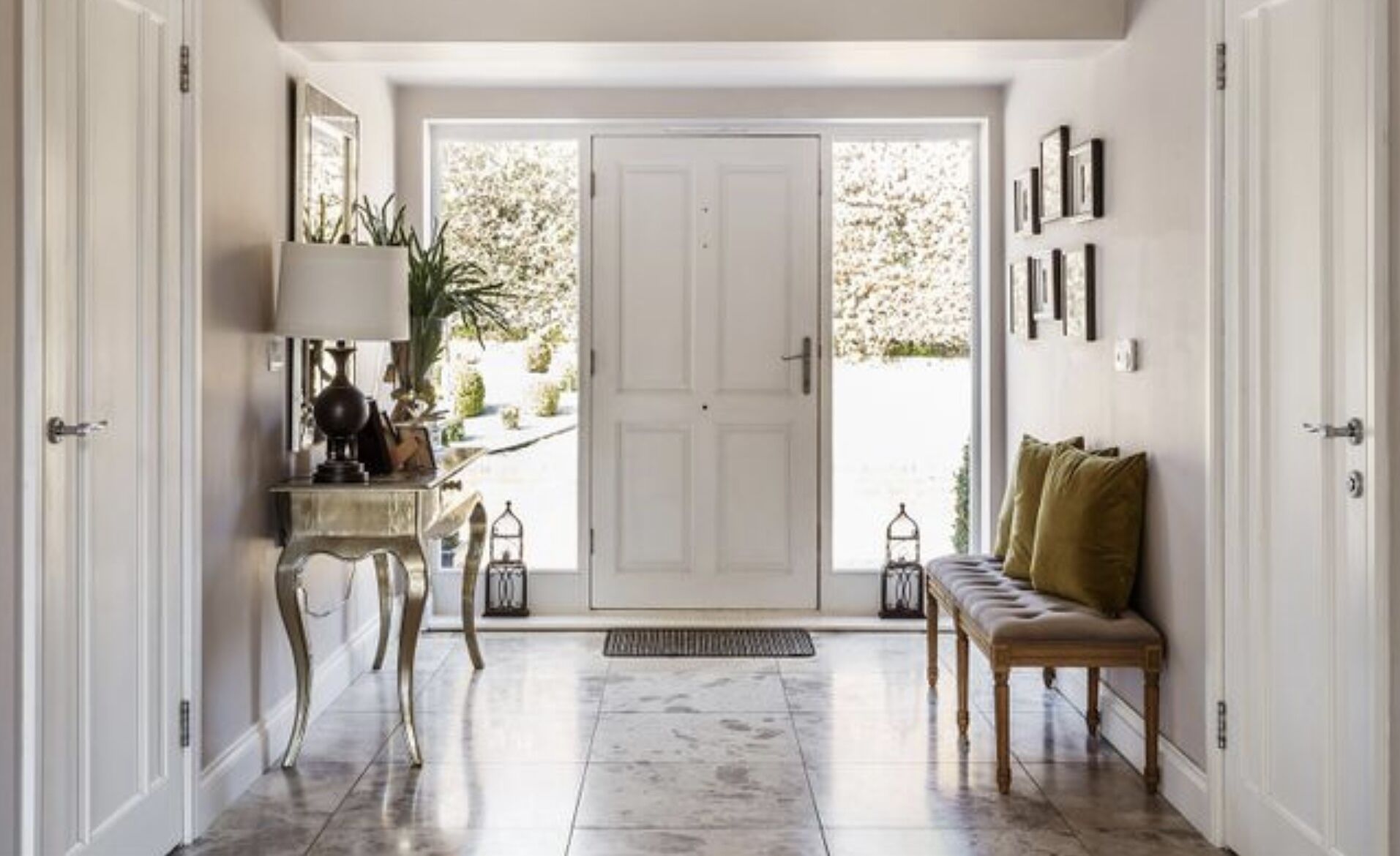A hallway with a white door, a bench, a lamp, and a potted plant.