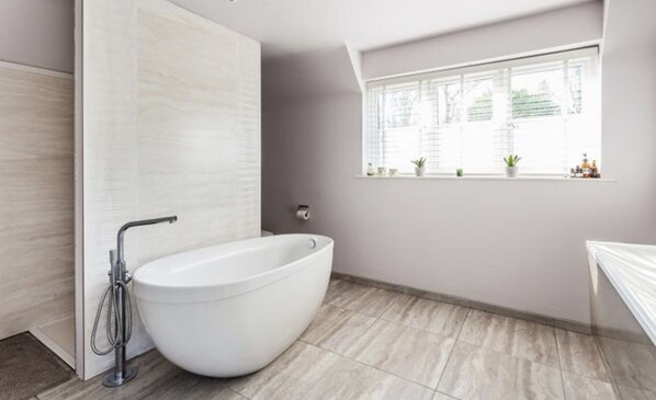 A modern bathroom with a freestanding bathtub, a window with plants, and a toilet paper holder.