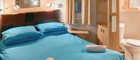 A neatly made bed with blue bedding, a wooden headboard, a bedside lamp, and a window with curtains.