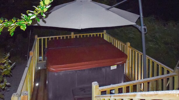 Une terrasse en bois avec un jacuzzi et un grand parasol.