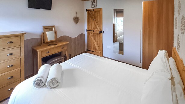 Een slaapkamer met een bed, een houten dressoir en een spiegel.