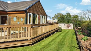 Een houten gebouw met terras, gazon en een boom met een rond bord.
