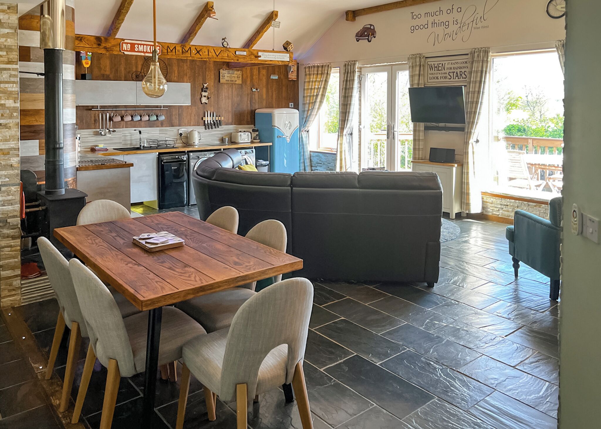 Un salon chaleureux avec une table à manger en bois, un canapé noir et un coin cuisine équipé d’une cuisinière et d’appareils électrom énagers modernes.