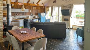 Een gezellige woonkamer met een houten eettafel, een zwarte bank en een keuken met een fornuis en moderne apparatuur.