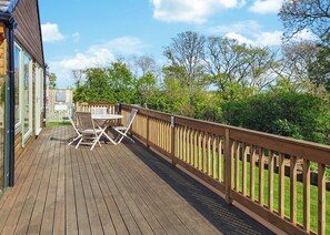 A wooden deck with a table and chairs, surrounded by a wooden fence and greenery.