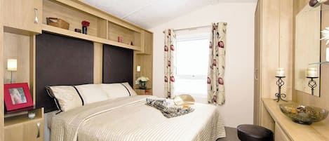 A bedroom with a bed, bedside tables, a dresser, a mirror, and a window with curtains.