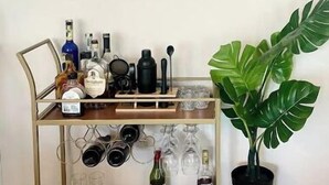 Une pièce dans laquelle on trouve un meuble mural servant de présentoir pour des bouteilles de vin et des verres, une plante en pot et trois œuvres d’art encadrées représentant des scènes abstraites et des animaux sauvages.