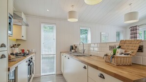 Moderni keittiö, jossa on valkoiset kaapit, puinen työtaso ja rottinkikori keittiösaarekkeella.