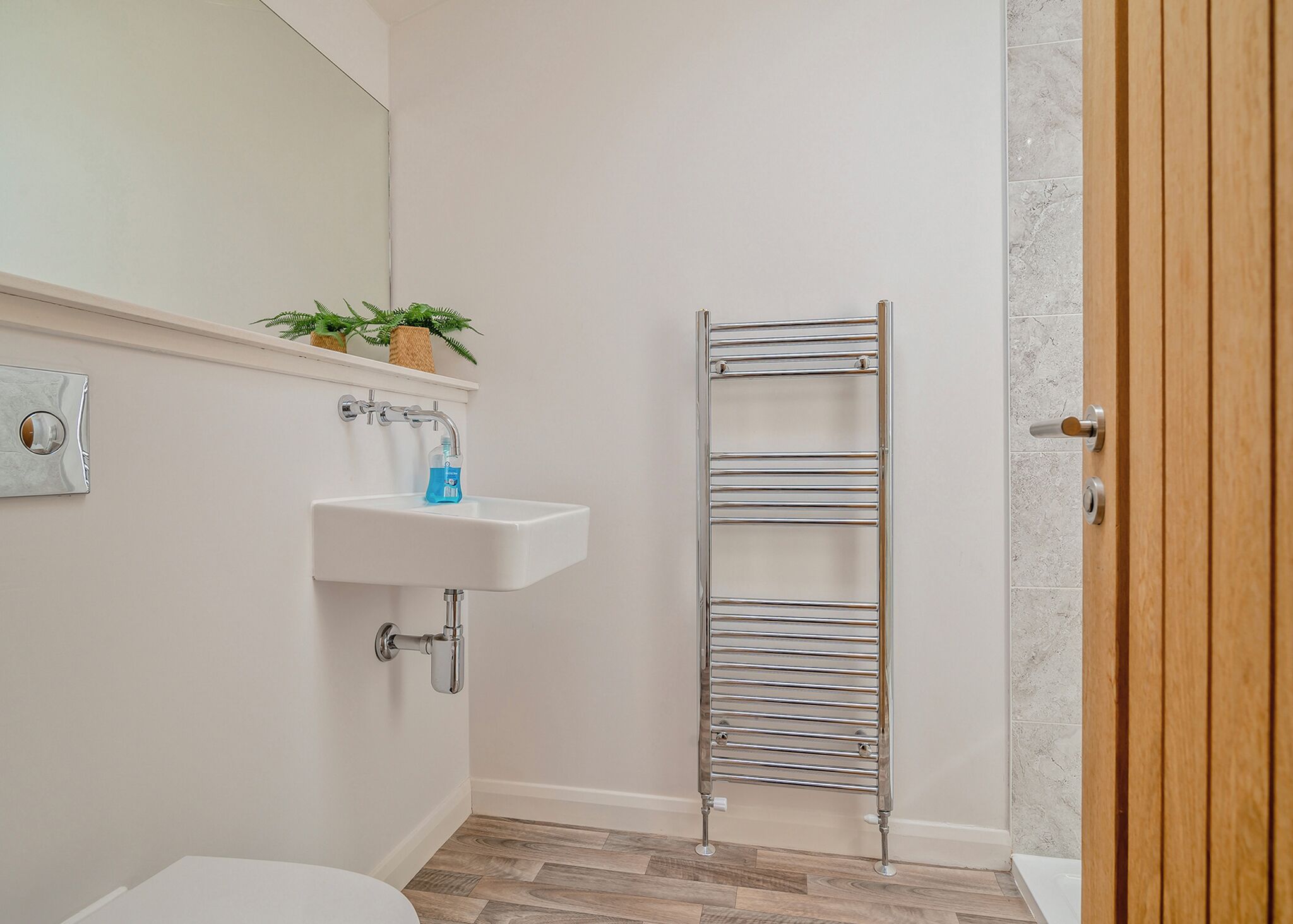 Ein Badezimmer mit einem weißen Waschbecken, einem Spiegel, einem Handtuchhalter und einer Holztür.
