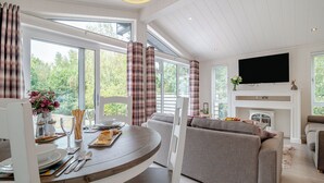 Moderni olohuone, jossa on takka, televisio ja ruokailutila, ja ruokapöytä on katettu kahdelle.