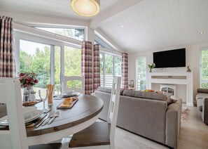 A modern living room with a fireplace, a television, and a dining area with a table set for two. - Rabbits Warren Lodge (Cannington)