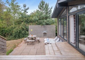A patio with a wooden table and chairs, a wooden deck, and a glass-enclosed room.