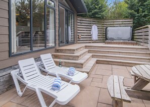 En udendørs terrasse med hvide liggestole, grill og træterrasse.