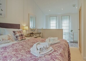 A hotel room with a large bed, a bedside table with a lamp, a mirror, and a view of the outside through large windows. - Rabbits Warren Lodge (Cannington)