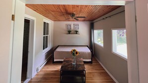 A bedroom with a bed, a ceiling fan, a window, and a small table with a vase. - Deer Hill Cottage on 5 Lake Chain (Haliburton)