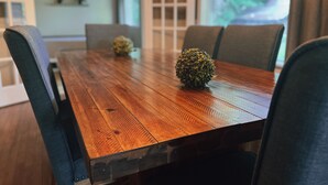 A wooden dining table with four chairs, two small potted plants, and a view of greenery outside. - Deer Hill Cottage on 5 Lake Chain (Haliburton)