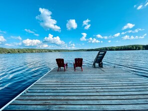 Un moll de fusta que s'endinsa en un llac tranquil, amb dues cadires vermelles i una cadira relaxant negra.