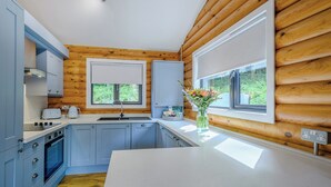 A modern kitchen with wooden walls, a white countertop, and a window with a view of greenery. - 1 bedroom accommodation in Annbank, Ayr (Annbank, Ayr)