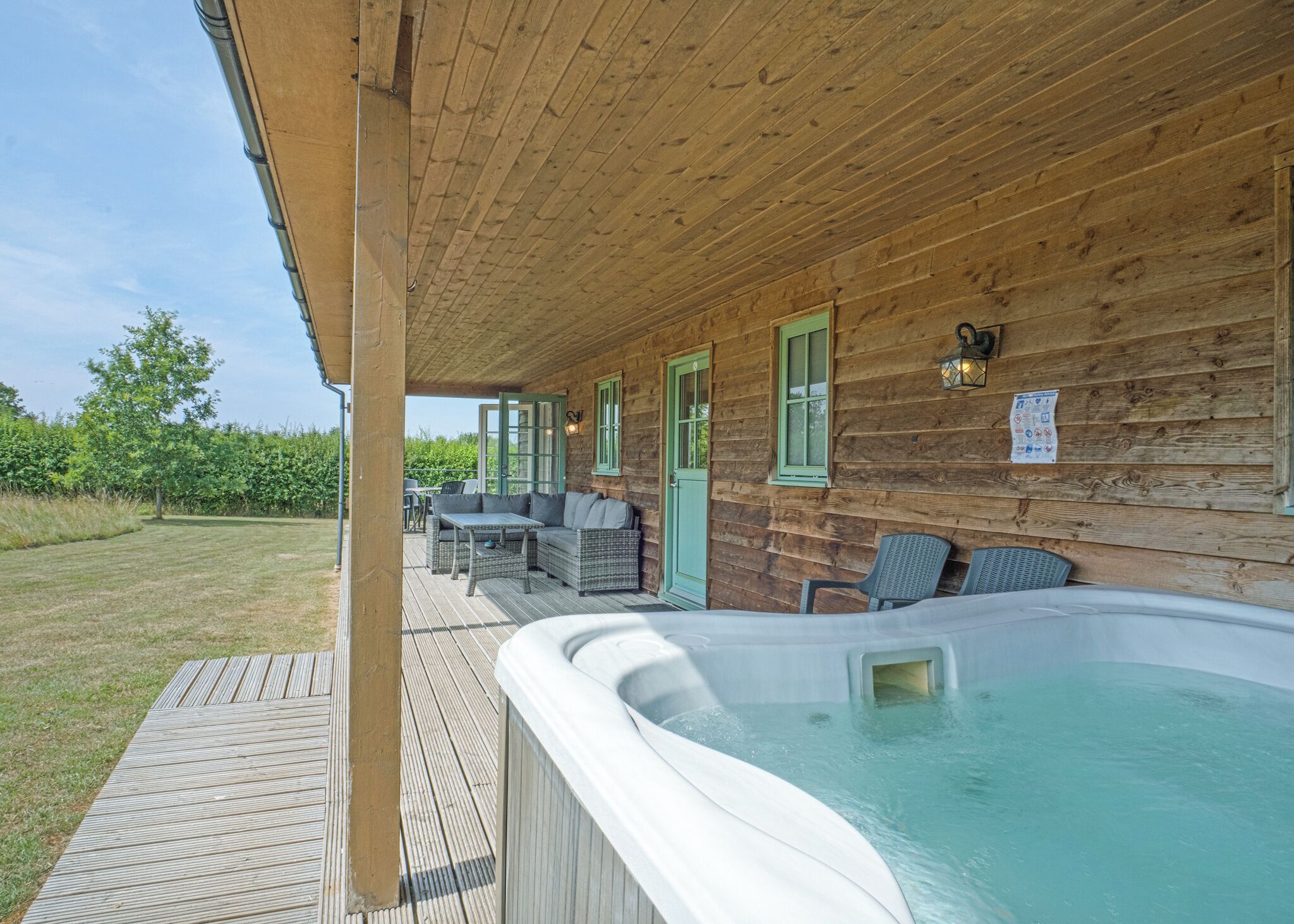 Eine Holzhütte mit Whirlpool, Sitzgelegenheit im Freien und einem Rasen.