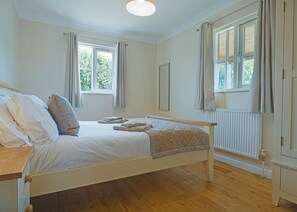Une chambre avec un lit simple, un plancher en bois, un radiateur et deux fenêtres avec des rideaux.