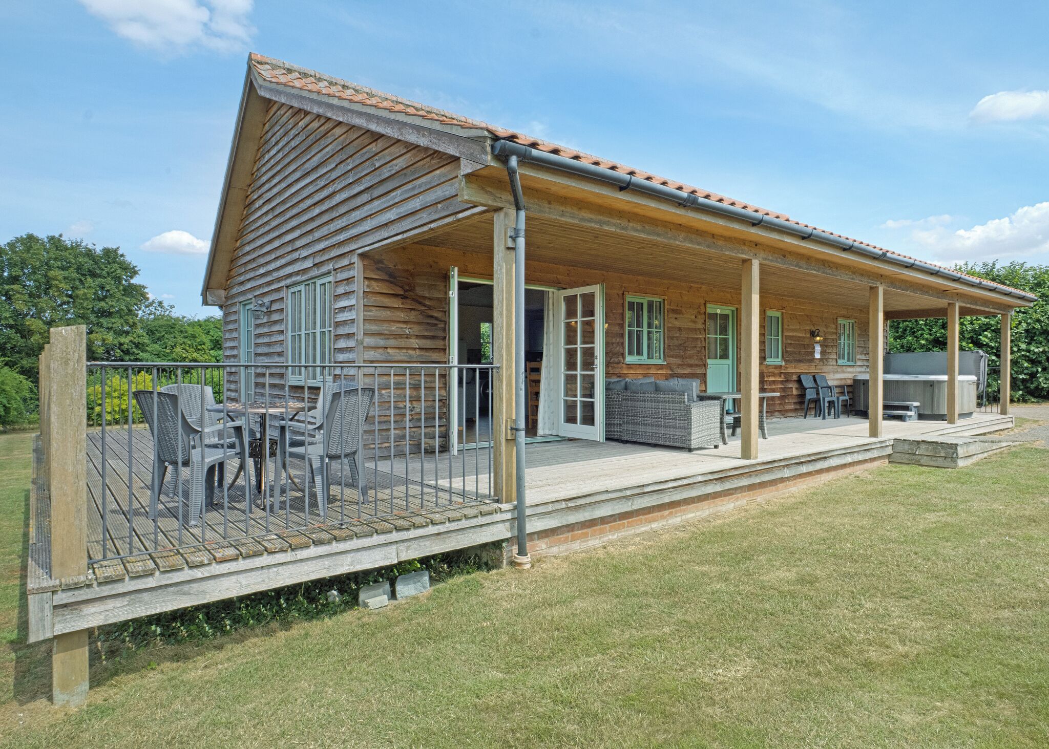 A wooden cabin with a covered patio, outdoor seating, and a hot tub.