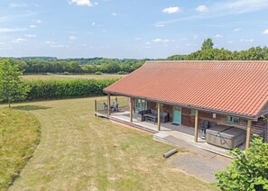 Une maison en bois avec un toit recouvert de tuiles rouges, une véranda abritée avec des meubles d’extérieur et une vue sur un champ verdoyant.