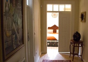 A hallway leading to a bedroom with a bed, a vase on a side table, and a painting on the wall.