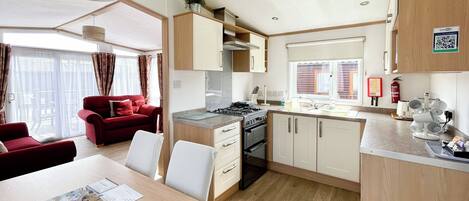 Una cocina compacta con electrodomésticos modernos, un comedor con mesa y sillas, y un sofá rojo en una habitación luminosa con ventanas amplias.