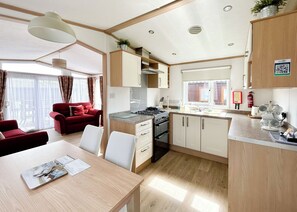 A compact kitchen with modern appliances, a dining area with a table and chairs, and a red sofa in a bright room with large windows.