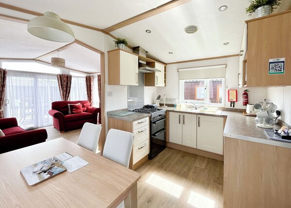 A compact kitchen with modern appliances, a dining area with a table and chairs, and a red sofa in a bright room with large windows.