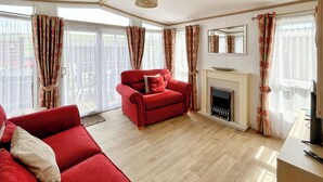 Ein Wohnzimmer mit einem roten Sofa, einem Kamin und großen Fenstern mit Vorhängen.
