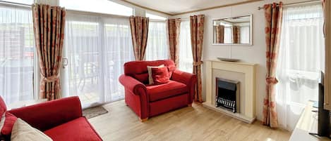 Una sala de estar con sofá rojo, chimenea y ventanas grandes con cortinas.