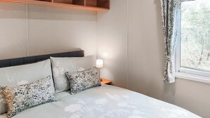 Una cama con ropa de cama floral, una lámpara de noche y una ventana con cortinas.