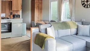 Una sala de estar moderna con un sofá gris, una mesa de centro de madera y una cocina con estufa y armarios.