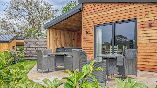 A modern wooden house with a patio, outdoor furniture, and a large sliding glass door. - A beautiful bespoke lodge perfect for a family escape. (Gledrid, Chirk)
