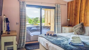 A bedroom with a bed, a nightstand, a lamp, a window with curtains, and a view of the outdoors. - A beautiful bespoke lodge perfect for a family escape. (Gledrid, Chirk)