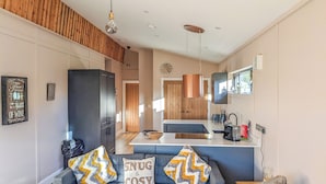 A modern living room with a grey sofa, two decorative pillows, a wooden ceiling, a kitchen area with a central island, and a dining table. - A beautiful bespoke lodge perfect for a family escape. (Gledrid, Chirk)