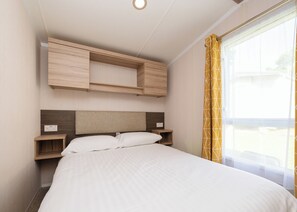 Un dormitorio con cama, cabecero de madera, mesitas de noche y una ventana con cortinas.