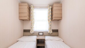 Quarto compacto de motorhome com duas camas, uma janela com cortinas e armários de madeira.