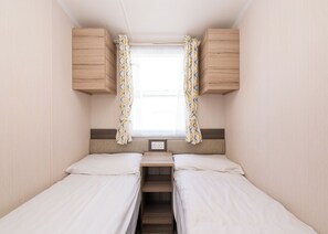 Un dormitorio de autocaravana compacto con dos camas, una ventana con cortinas y armarios de madera.