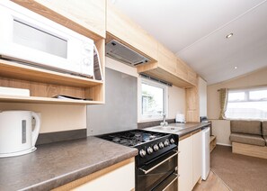 A compact kitchen with a stove, microwave, and sink, wooden cabinets, and a window. - 2 bedroom accommodation in Looe (Looe)