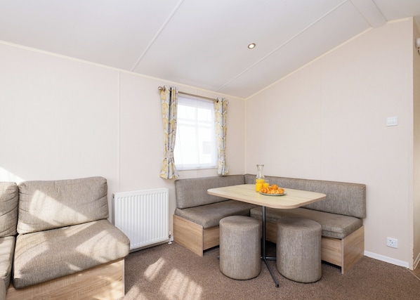 Ein gemütliches Zimmer mit einer Eckcouch, einem kleinen Tisch mit einem Glasbehälter und Orangensaft sowie einem Heizkörper.