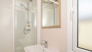 A bathroom with a glass-enclosed shower, a white sink, and a mirror above it.