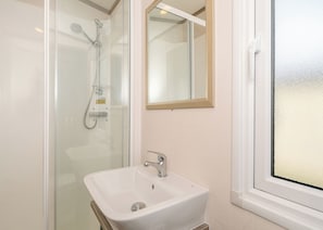 Un baño con ducha de vidrio, un lavabo blanco y un espejo encima.