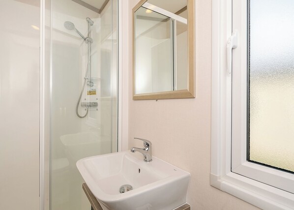 A bathroom with a glass-enclosed shower, a white sink, and a mirror above it.