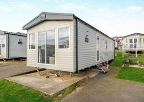 Une maison mobile de plain-pied dotée d’un patio, d’un espace extérieur couvert avec des sièges et d’une fenêtre visible.